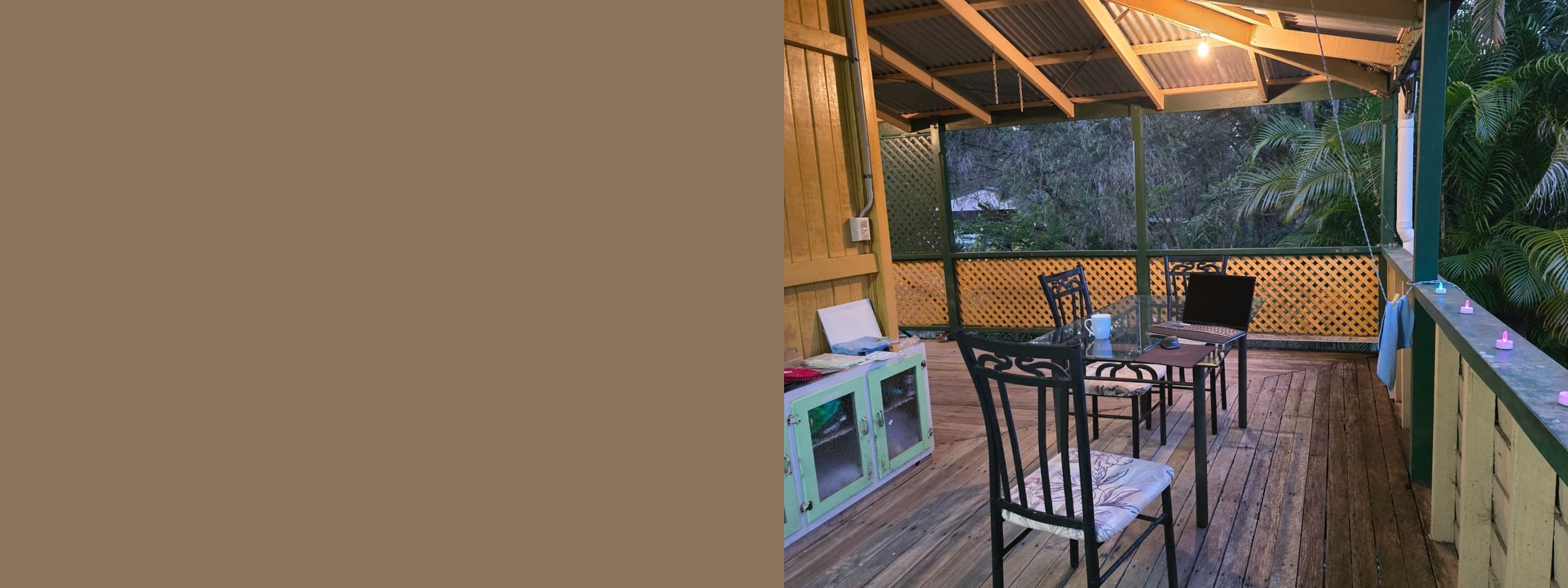 Laptop and mug on a glass table on a wooden deck overlooking lush tropical greenery.