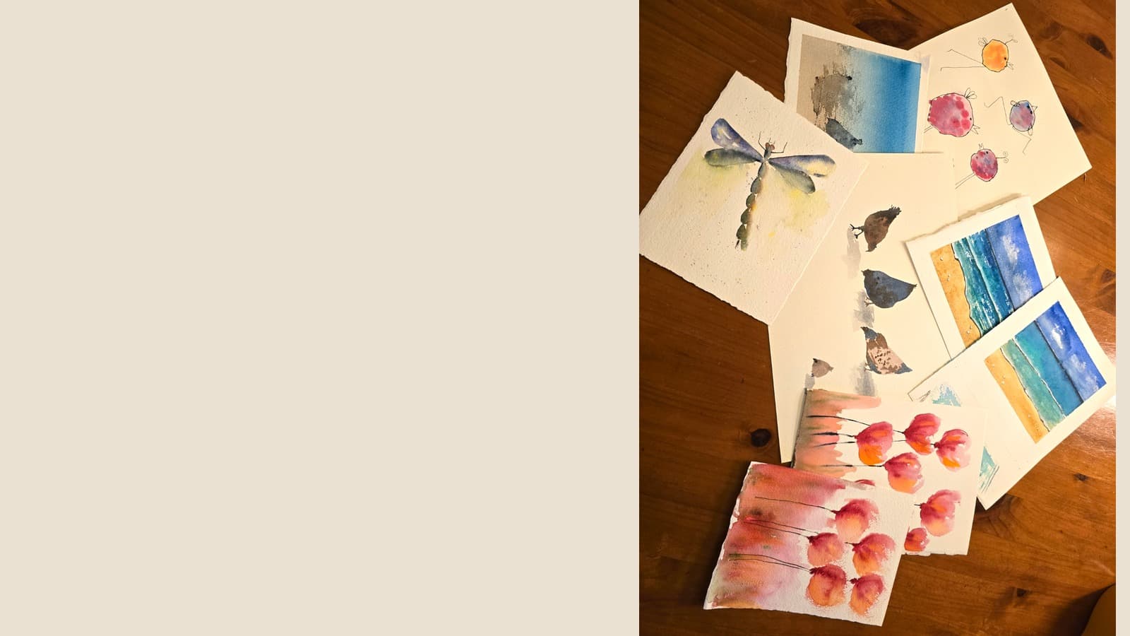 Watercolor paintings of a dragonfly, flowers, birds, and beach scenes scattered on a wooden table.
